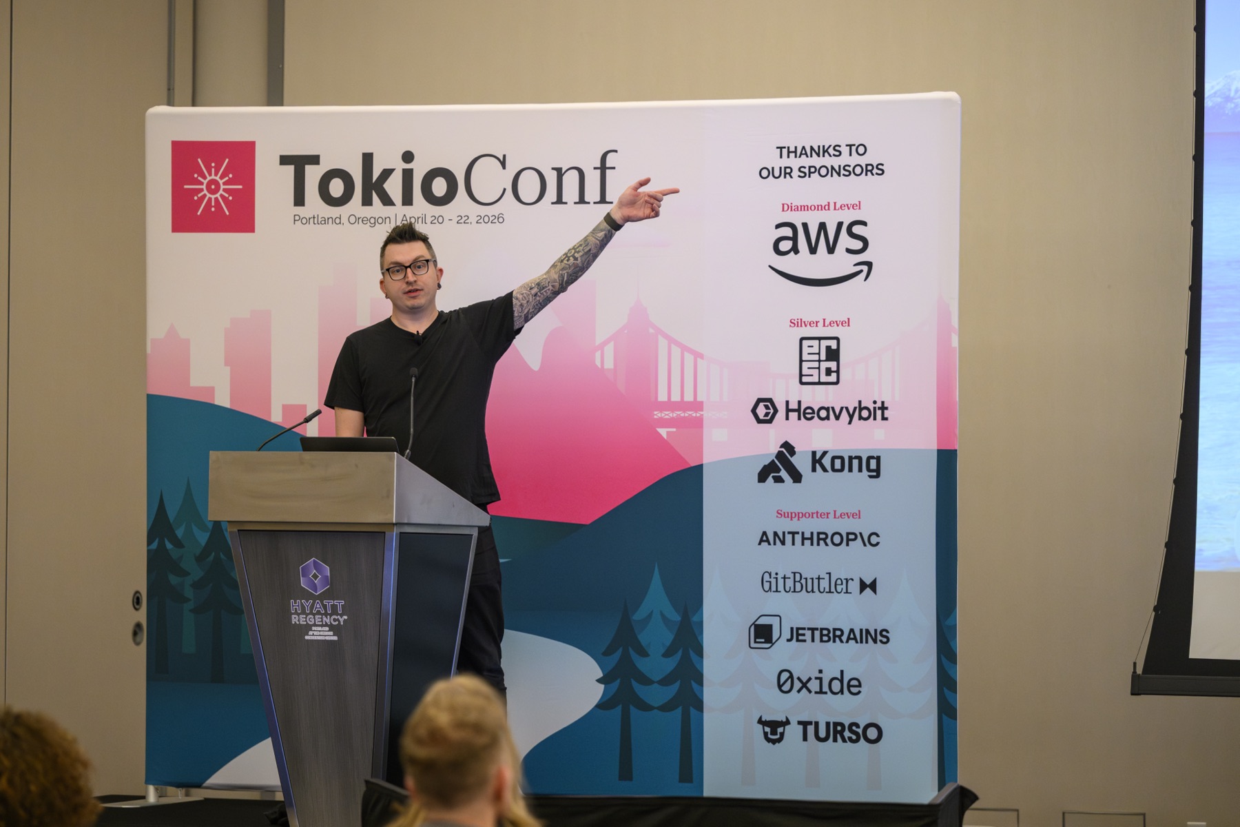 A presenter pointing at the TokioConf backdrop